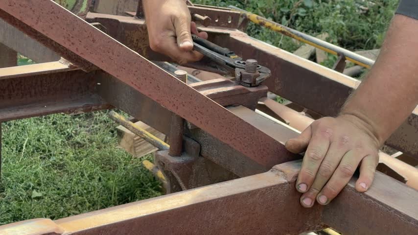 Close view of a person using an adjustable wrench to turn a nut on a rusted steel frame outdoors.