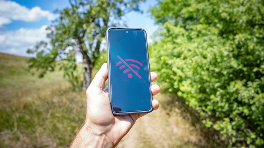 Hand Holding Smartphone with No Signal Icon on Screen Outdoors in Nature