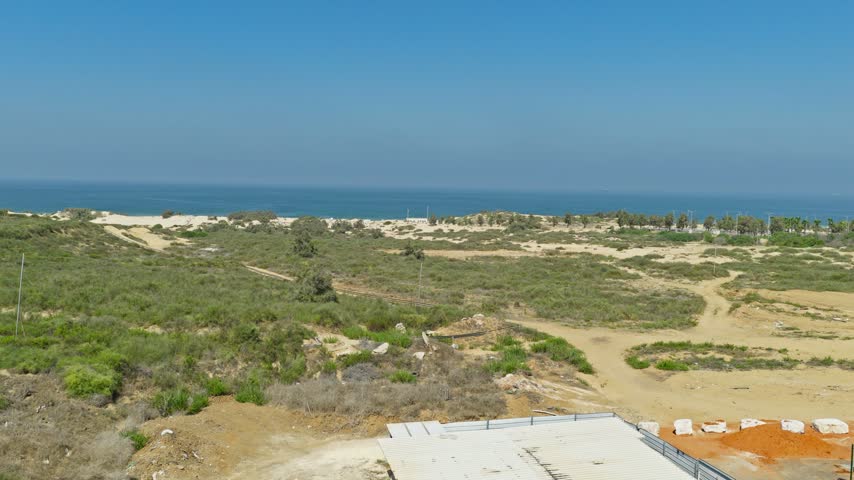 Aerial drone shot over green vegetation and sandy tracks of Nitzanim Sand Dunes Nature Reserve with the blue Mediterranean Sea and clear sky in the background near Ashdod Israel.