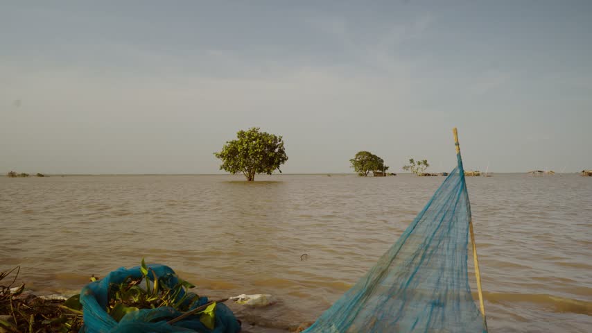 View of a flooded river bank with blue fishing nets spread along the muddy water side.