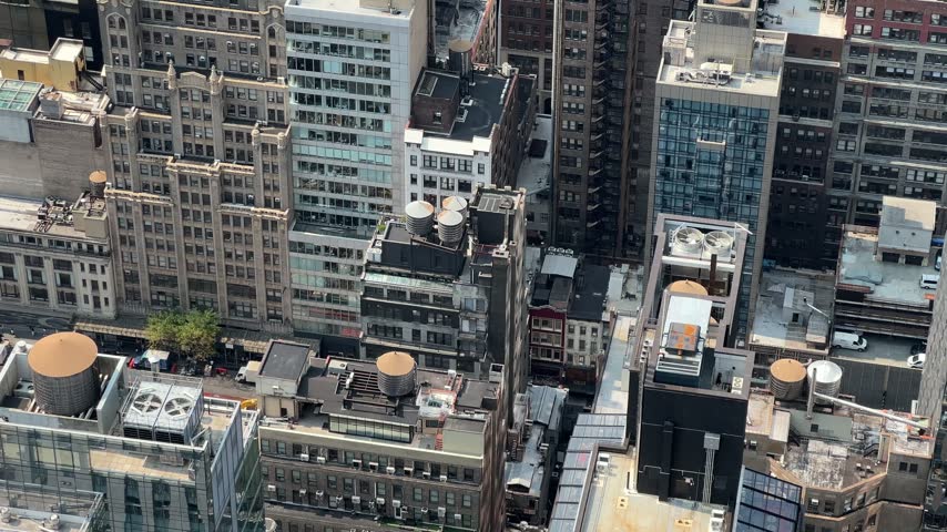 Tall downtown buildings crowd a city block, revealing rooftop water towers, HVAC units, and narrow streets below from above.