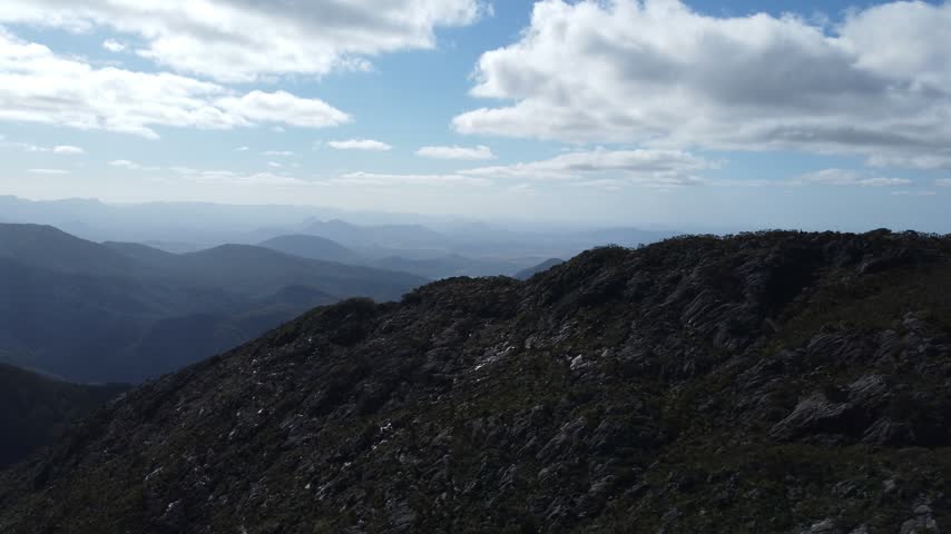 Breathtaking aerial view from a rocky mountain peak revealing vast mountain ranges and a distant lake under a cloudy sky