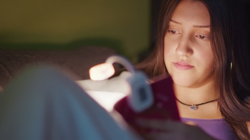 Cinematic close-up of a young girl reading a book at night, illuminated by a warm reading lamp. Cozy, intimate atmosphere for family, education and lifestyle projects