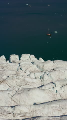 Massive Glacier Flows Toward The Sea Along Rugged Arctic Coastline With Sailboat In Greenland. Vertical, High-angle Shot