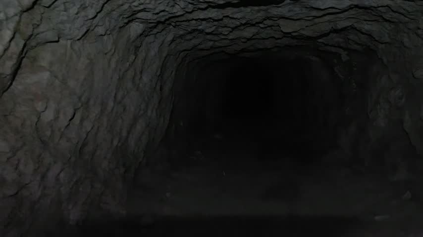 Camera pan showing dark cave tunnel and revealing illuminated rocky ceiling with a powerful flashlight, geology exploration concept.