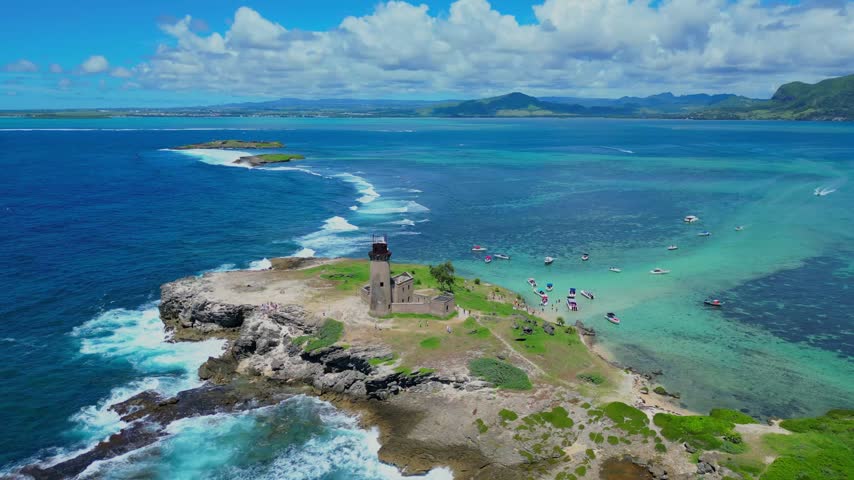 Aerial view of the historic lighthouse on the rocky island of Ile aux Fouquets surrounded by turquoise lagoon waters and boats in Mauritius.