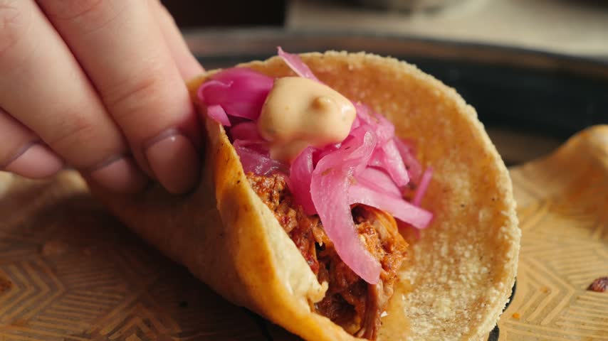 Hand picking up a freshly prepared taco from a serving plate. Close-up of a traditional Mexican street food with fresh ingredients, ready to eat.