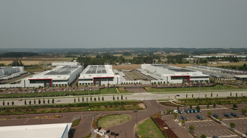 View of large data center complexes in Hillsboro, Oregon, featuring industrial buildings and rooftop cooling systems supporting cloud computing, AI, and digital infrastructure. Wide aerial shot.