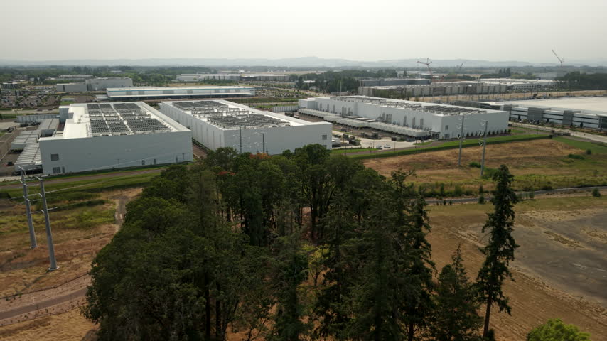 View of large data center complexes in Hillsboro, Oregon, featuring industrial buildings and rooftop cooling systems supporting cloud computing, AI, and digital infrastructure. Wide drone orbit.