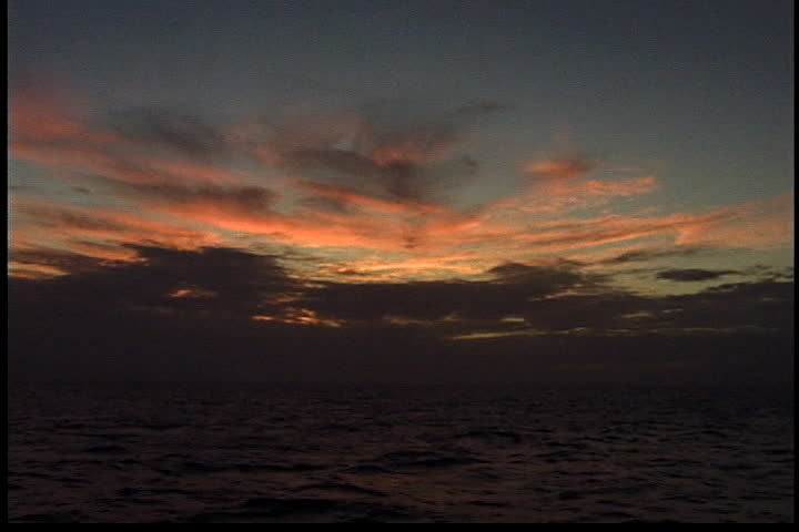 Sun shines through dramatic dark and orange clouds above Atlantic Ocean.