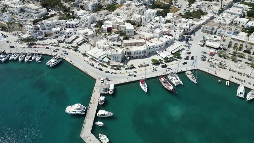 Drone close-up of the iconic blue-domed Greek Orthodox church in Adamantas, Milos, surrounded by whitewashed houses and dry Cycladic hills.