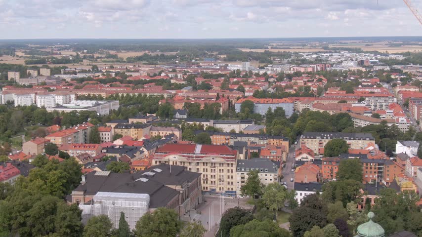Wide aerial of dense red-tiled roofs in Uppsala, Sweden. Neoclassical building under white renovation sheeting; green copper dome edge.