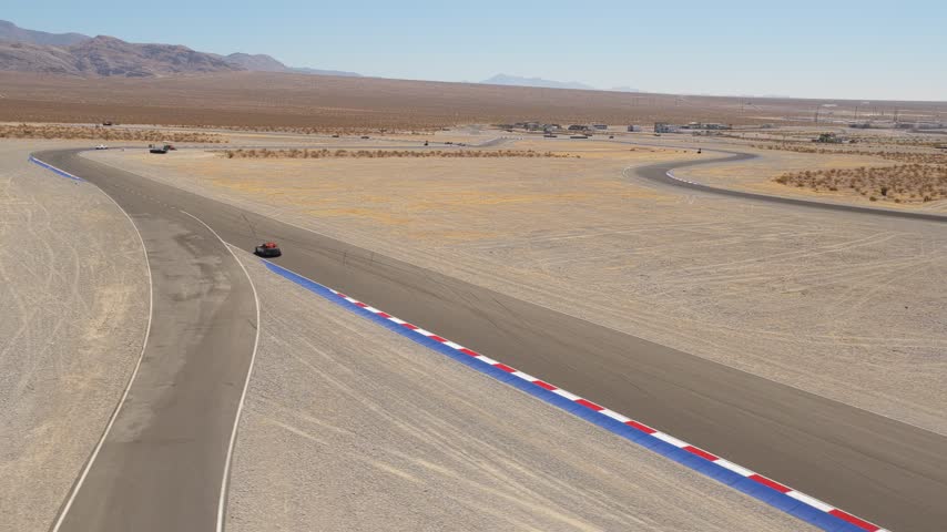 Aerial view of racing cars moving around a desert circuit corner
