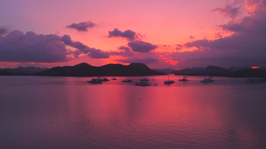 Vivid pink and orange sunset reflecting across Coron Bay with anchored boats and a waterfront pavilion