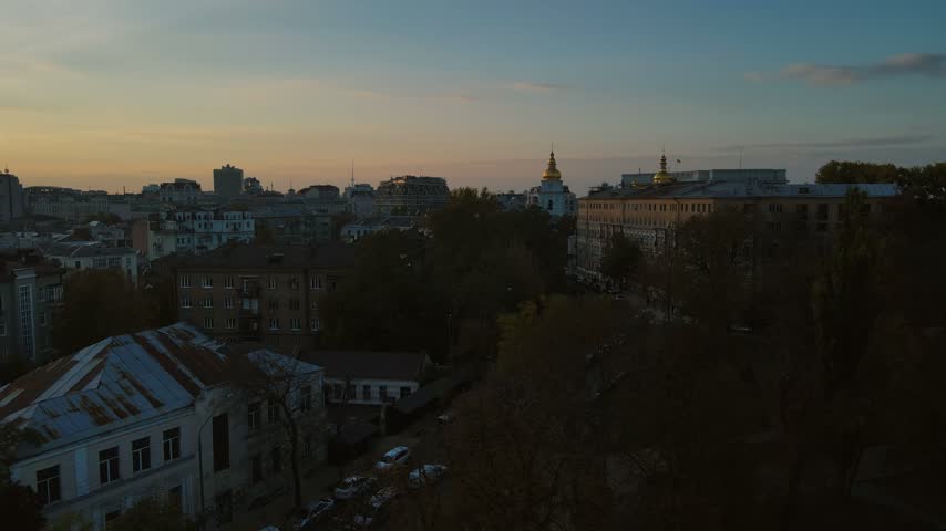 Aerial view of historic Kyiv street and rooftops toward monastery at sunset