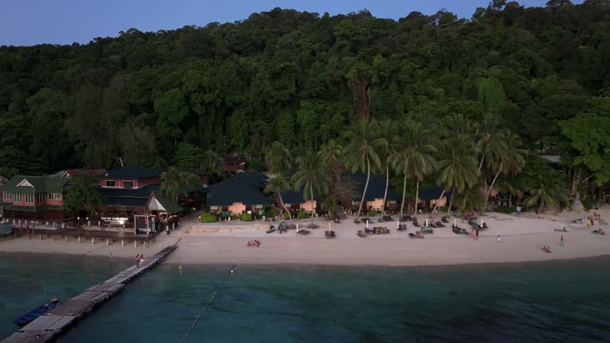 Aerial view of Perhentian Islands resort with palm trees, sandy beach, and wooden pier along the coastline in Terengganu, Malaysia.