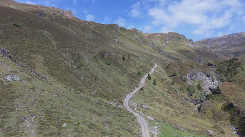 Drone approach along a winding mountain path beside a rocky stream gorge. Tyrol, Austria. Natural daylight.