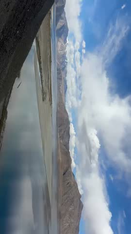 High-altitude landscape view of famous blue lake waters mirroring mountains and sky on a sunny day in Ladakh, India.