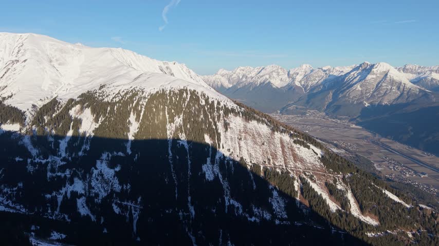 Drone pan from a sunlit snowy mountain slope to a wide alpine valley in Tyrol Austria.