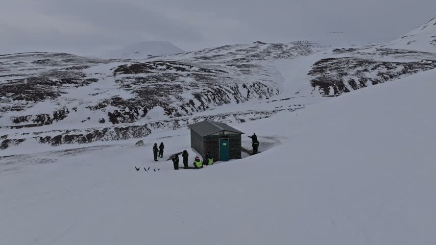 Aerial view of a small cabin in a vast snowy landscape with people standing outside in Pyramiden, Svalbard, Svalbard and Jan Mayen.