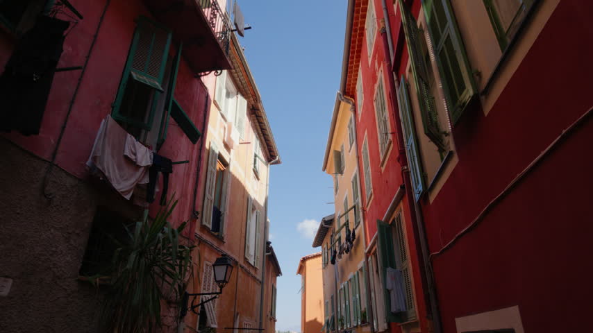 Looking up at colorful old buildings and open shutters in a narrow Villefranche-sur-Mer street