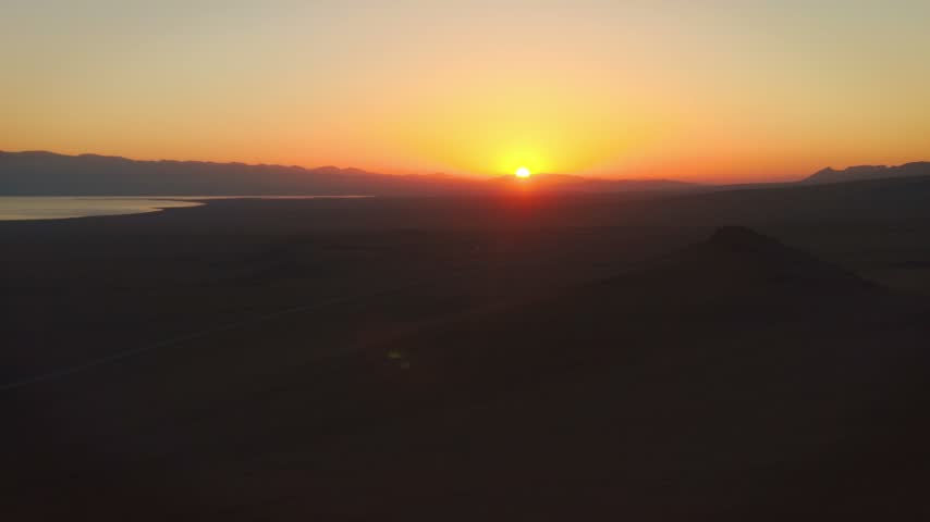 Aerial silhouette of hikers standing on mountain pass near communication tower watching golden sunset over Song-Kul Lake, Kyrgyzstan