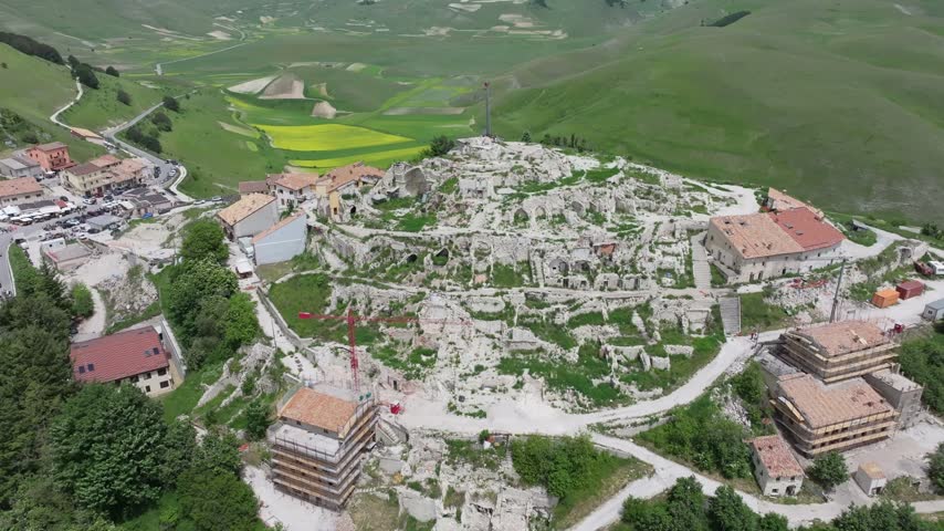 Aerial view of the historic village of Castelluccio showing earthquake ruins, reconstruction efforts, and surrounding green hills in Castelluccio, Umbria, Italy.