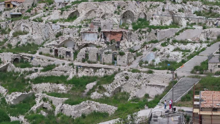 Aerial view of the earthquake-damaged ruins of Castelluccio with stone walls, overgrown vegetation, and stone staircases in the hillside village of Castelluccio, Umbria, Italy.