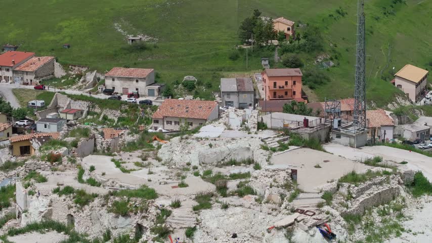 Aerial view of the earthquake-damaged village of Castelluccio with ruins and rubble surrounded by green hills in Castelluccio, Umbria, Italy.