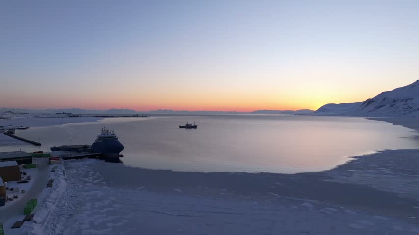 Aerial view of a ship docked at the icy harbor of Longyearbyen with a vessel in the bay and snow-covered mountains under a twilight sky in Longyearbyen, Svalbard, Svalbard and Jan Mayen.