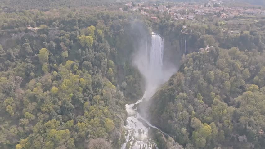 Aerial view of the cascading Marmore Falls surrounded by lush green forests and rocky cliffs in Terni, Umbria, Italy.