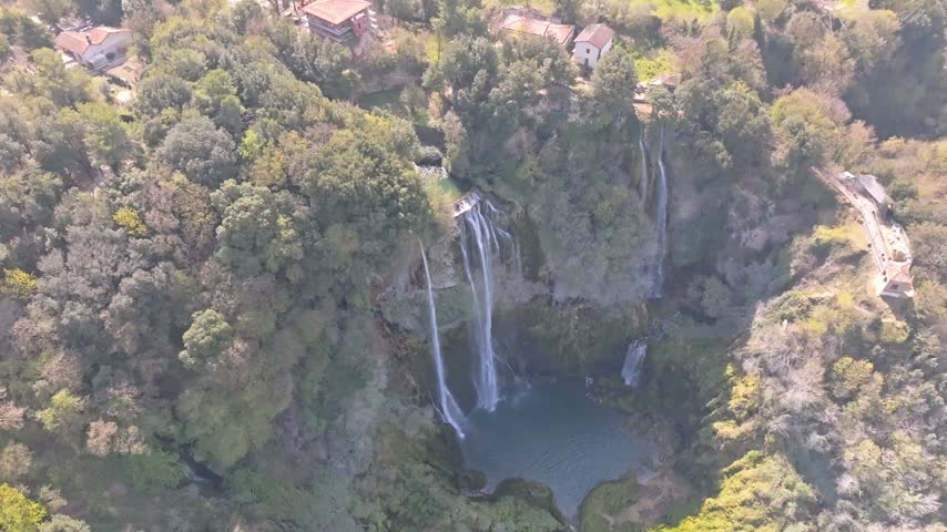 Aerial view of the cascading waters of Marmore Falls surrounded by lush green forests and rocky cliffs in Terni, Umbria, Italy.