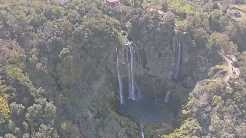 Aerial view of the cascading Marmore Falls surrounded by lush green forests and rocky cliffs in Terni, Umbria, Italy.
