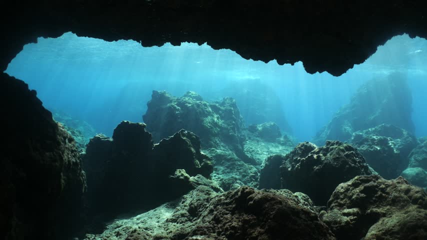 underwater landscape scenery with rocks and blue water sun beams and sun rays with fish and waves