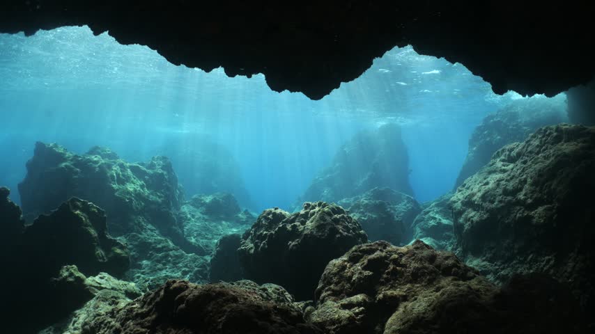 underwater landscape scenery with rocks and blue water sun beams and sun rays with fish and waves