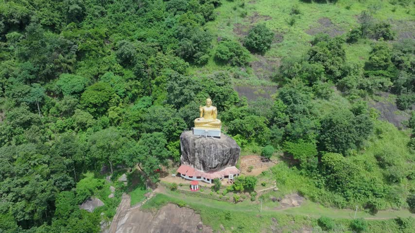 Aerial view of the golden Buddha statue perched on a large rock surrounded by lush green forest in Kandy, Central Province, Sri Lanka.