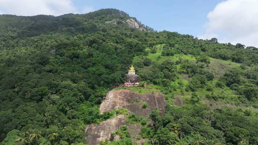 Aerial view of the golden Buddha statue at Bahirawakanda Vihara perched on a rocky cliff surrounded by lush green tropical forest in Kandy, Central Province, Sri Lanka.