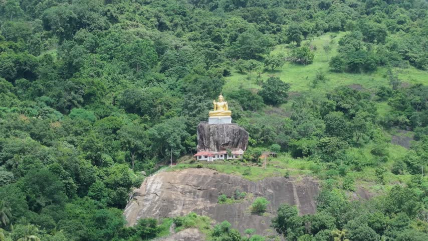 Aerial view of the golden Buddha statue perched on a rocky outcrop surrounded by lush green forest in Kandy, Central Province, Sri Lanka.