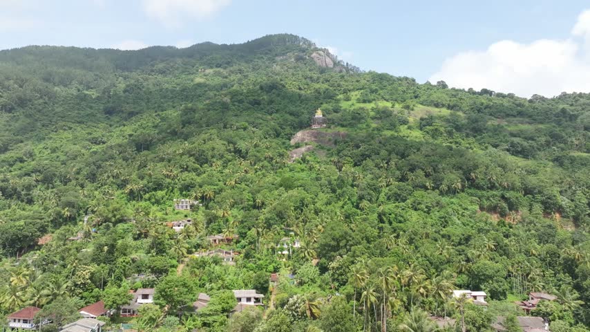 Aerial view of the Bahirawakanda Vihara Buddha Statue nestled on a lush green hillside with tropical trees and residential houses in Kandy, Central Province, Sri Lanka.