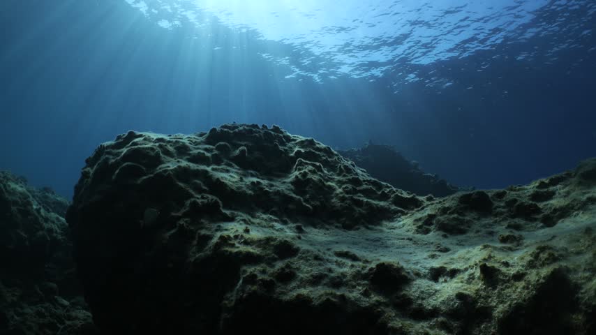 underwater landscape scenery with rocks and blue water sun beams and sun rays with fish and waves
