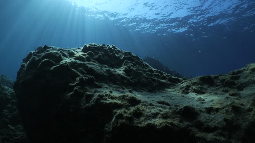 underwater landscape scenery with rocks and blue water sun beams and sun rays with fish and waves