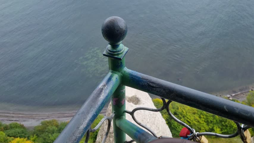 White chalk cliffs and forested slopes stretch along the Baltic coast beyond the iron railing of a clifftop viewpoint on Ruegen in Germany.
