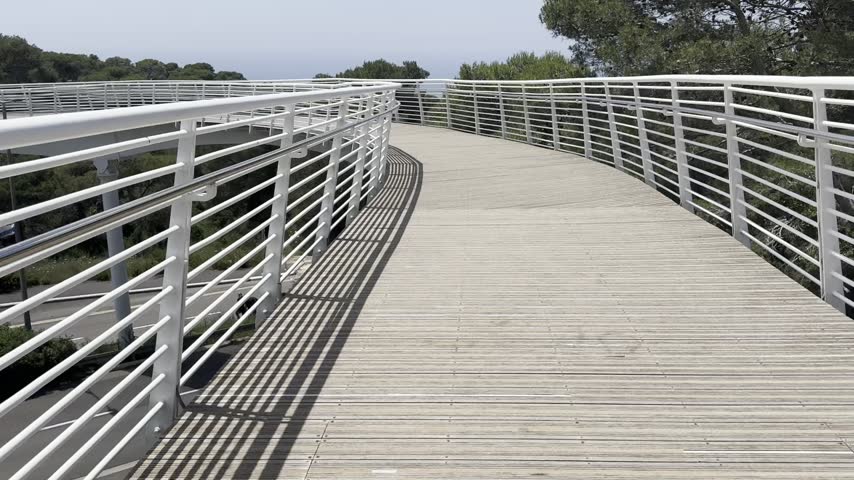 Haifa, Israel. Camera moves along a modern pedestrian bridge over a highway leading toward the Mount Carmel nature reserve.