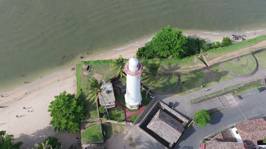 Aerial view of the historic Colombo Lighthouse surrounded by palm trees and coastal fortifications near the beach in Colombo, Western Province, Sri Lanka.