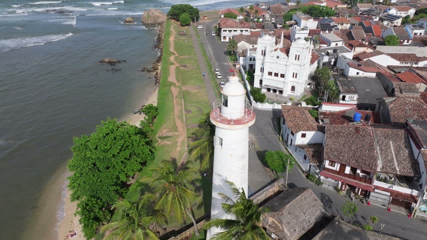 Aerial view of Colombo Lighthouse, the historic white church, and coastal road along the ocean in Colombo, Western Province, Sri Lanka.