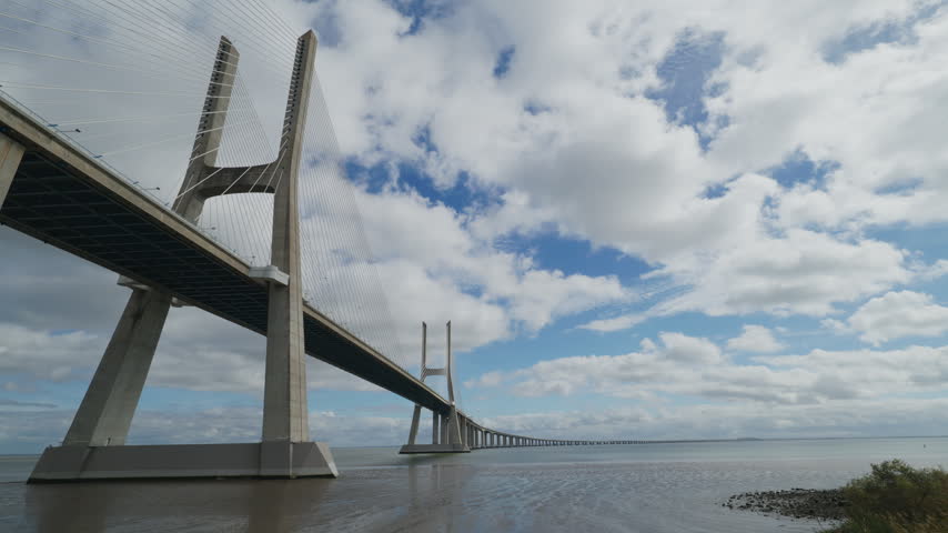 Vasco Da Gama Bridge Spans Wide River Under Cloudy Sky, Showing Modern Cable Stay Engineering And Calm Water Below. Bridge Arcs Toward Horizon In Lisbon.