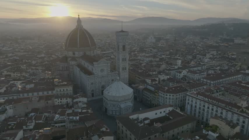 Aerial view of Florence Cathedral and the Baptistery at sunrise with golden light over the historic city rooftops in Florence, Tuscany, Italy.