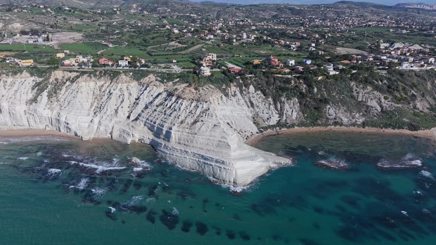 Aerial view of Stair of the Turks white marl cliffs along the Mediterranean coast with turquoise waters and nearby residential buildings in Realmonte, Sicily, Italy.