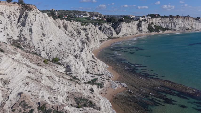 Aerial view of the white marl cliffs of Stair of the Turks along the coastline with turquoise sea and sandy beach in Realmonte, Sicily, Italy.