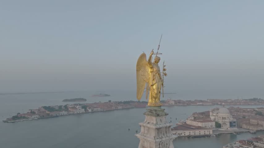 Aerial view of the golden angel statue atop the Campanile di San Marco overlooking the historic city skyline and the Venetian lagoon in Venice, Veneto, Italy.